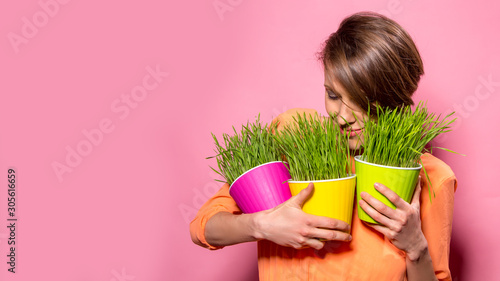 Young lady with wheatgrass in flower pots over bright pink background photo