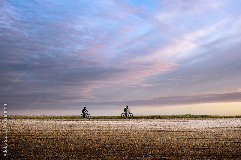 two cyclists riding under a beautiful sunset two cyclists riding under a beautiful sunset