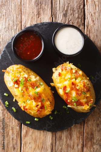 Baked potatoes with cheddar cheese, green onions and bacon close-up. Vertical top view