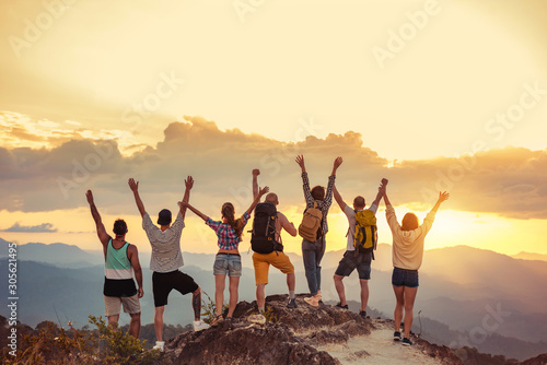 Happy friends stands with raised arms against sunet mountains