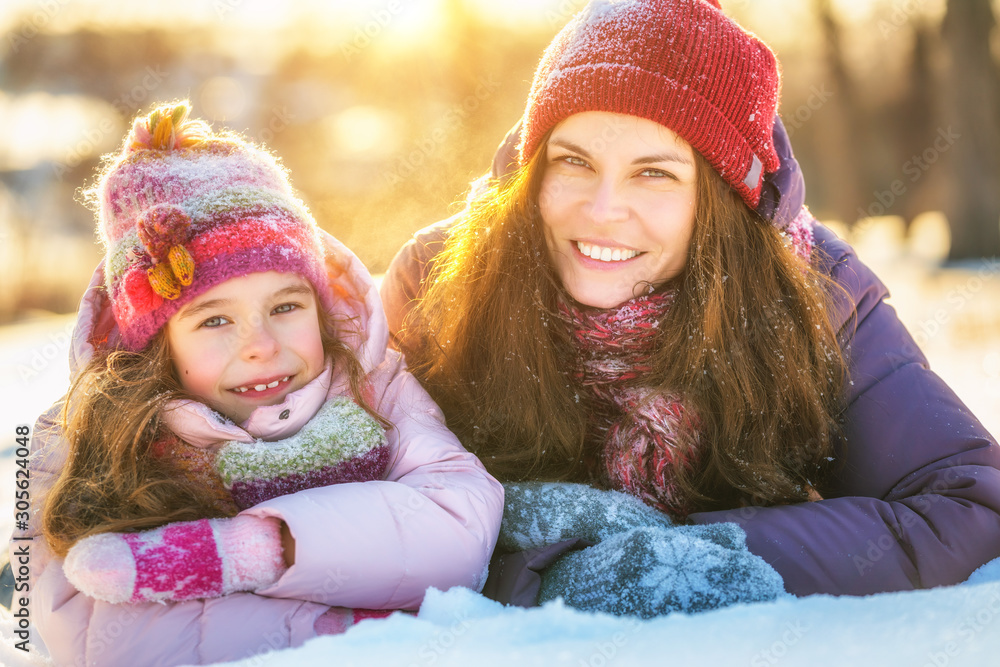 Little girl and her mother playing outdoors at sunny winter day. Active winter holydays concept.