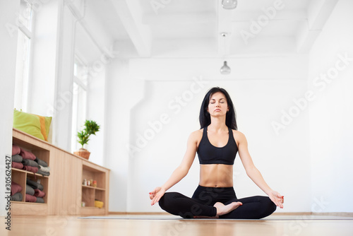 Woman exercising easy yoga sitting asana with closed eyes. Meditation alone in yoga school for restoration of mental balance and internal strength. Concept of sport in daily life. Light background