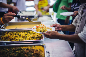 The hands of the needy holding a container to receive free charity food from volunteers : the concept of food assistance
