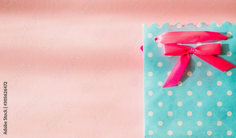 Blue gift bag with polka dots and with a bow on a pink background. View from above. The shadow from the sun is falling