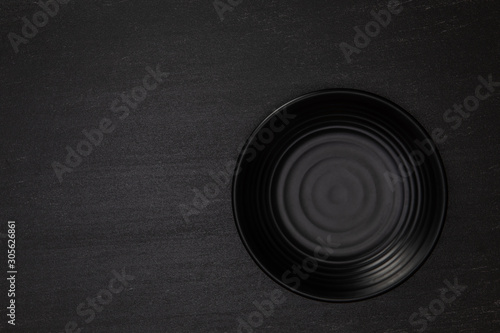 Empty blank black ceramic round bowl on black stone blackground with copy space, Top view of traditional handcrafted kitchenware concept