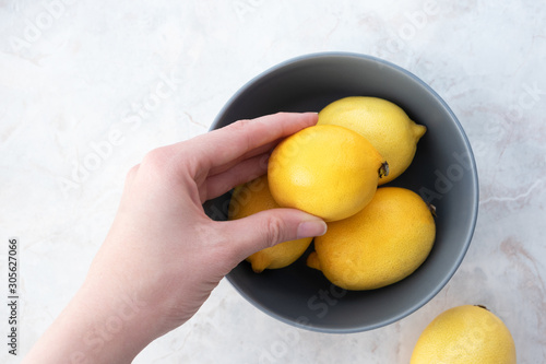 Hand hold raw fresh yellow lemon in bowl on marble table. Organic ripe citrus fruits