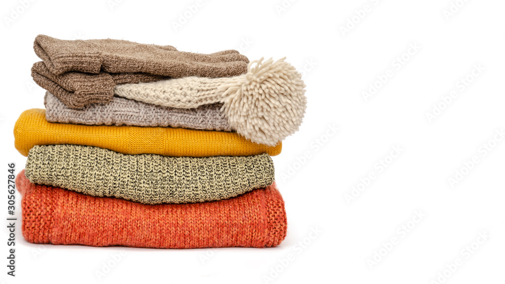 A stack of folded knitted warm women sweaters, hat and gloves on a white background. Season of warm clothes. Time to keep warm. Closeup. Copy space