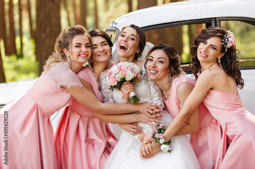 Wedding photography of happy bride and bridesmaids in pink dresses embracing with smile on wedding day