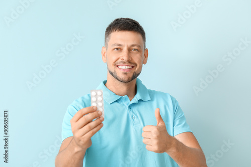 Man with pills showing thumb-up on color background