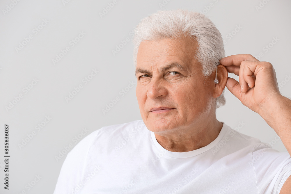 Mature man with hearing aid on light background Mature man with hearing aid on light background