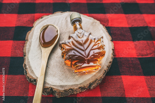 Maple syrup bottle Quebec cultural food traditional harvest top view on buffalo dining tablecloth background. Canada grade A amber sweet liquid in wooden spoon from sugar shack cabane a sucre farm. photo