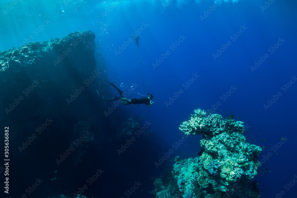 Obraz premium Free diver dive in deep ocean, underwater view with rocks and corals. Freediving