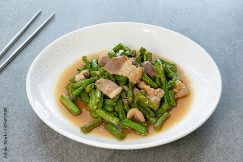 Fried yardlong beans with streaky pork in white dish on concrete table.