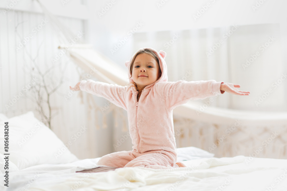 child in plush pajamas on bed, light bedroom child in plush pajamas on bed, light bedroom