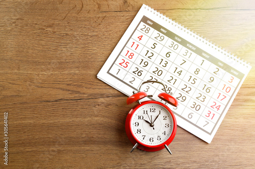 Calendar and alarm clock on wooden table, flat lay. Space for text