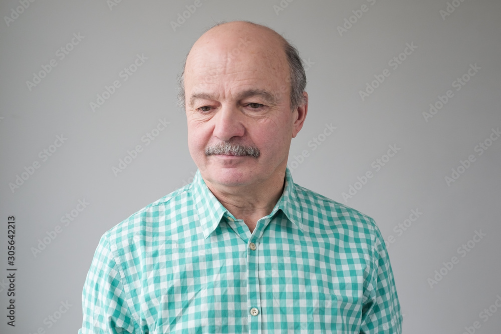 Fototapeta premium Close up studio shot of senior hispanic bald man with mustache looking down being upset with news.