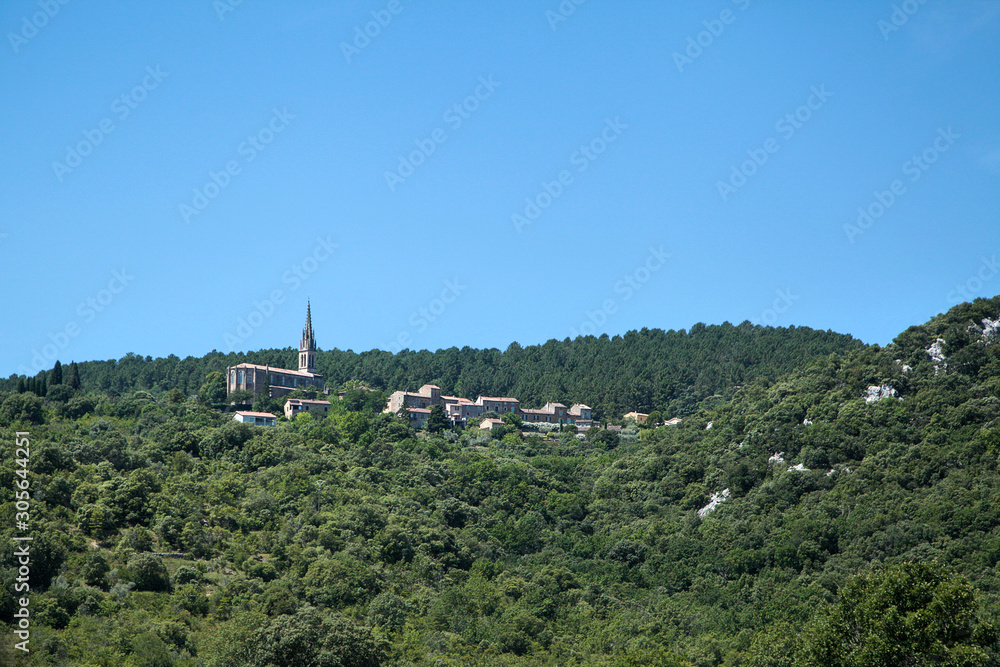 French countryside landscape at sunny summer day. Catholic church (église Saint-Pierre-ès-Liens) among green hills in village of Banne, Ardeche, Rhone-Alpes, southern France