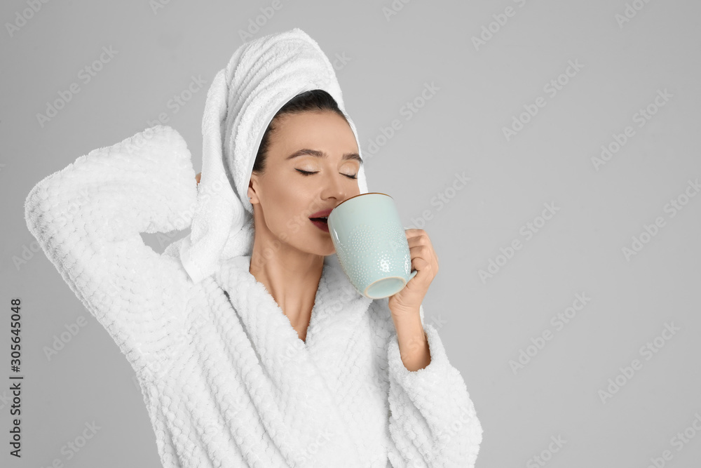 Beautiful young woman in bathrobe with cup of coffee on light grey background. Space for text Beautiful young woman in bathrobe with cup of coffee on light grey background. Space for text