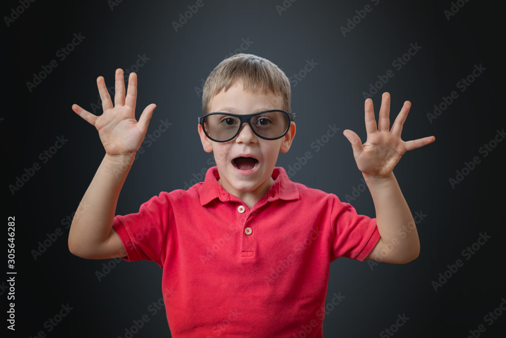 A boy with hands raised plays a monster or reacts to a scary moment in a movie. There are 3d glasses on the eyes. Black bacgkround..