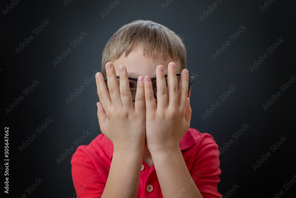 The boy peeks through his fingers. Watching a scary movie with 3d glasses. The boy peeks through his fingers. Watching a scary movie with 3d glasses.