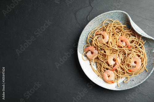 Plate of tasty buckwheat noodles with shrimps on black table, top view. Space for text