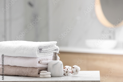 Clean towels, spa stones and soap dispenser on table in bathroom. Space for text