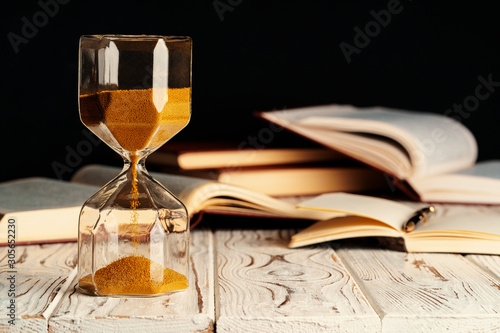 Sandglass on wooden table with opened book close up