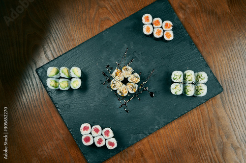 Set of maki roll sushi with cucumber, salmon, eel, tuna on black sltae board on wooden background. Japanese cuisine. Top view