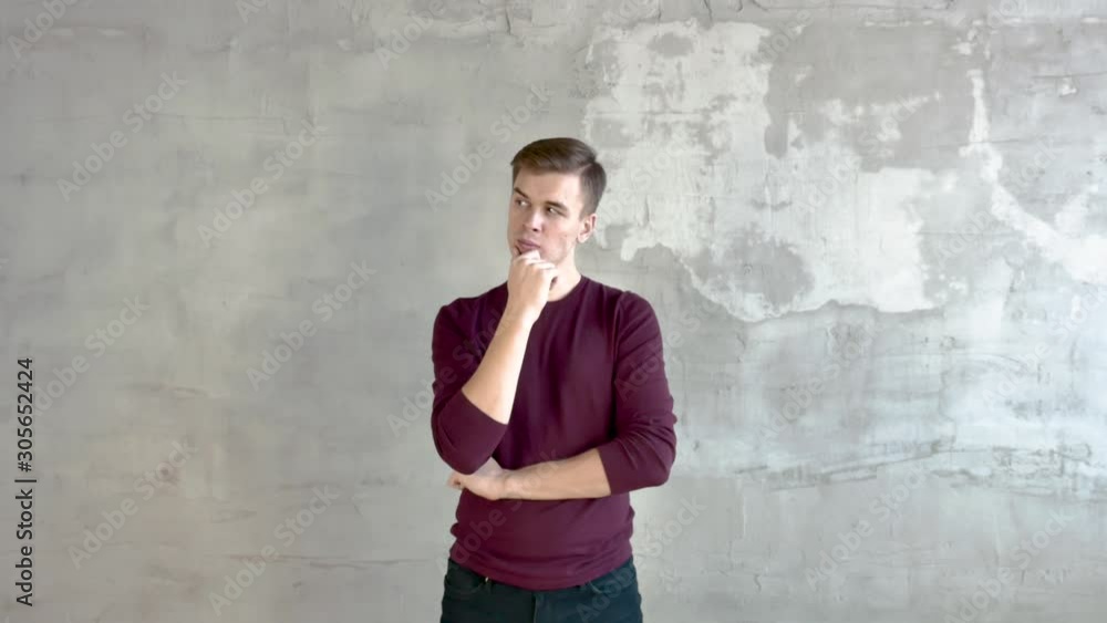 Young man against gray wall short haircut burgundy jumper looks left up right rubbing his chin loose local for inscriptions left to right medium shot