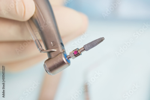 During the operation, the dentist holds implantation tools with a titanium implant