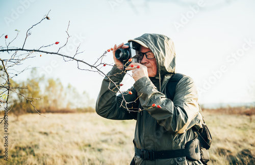 Old man taking photo in nature. Man photographing autumn forest.