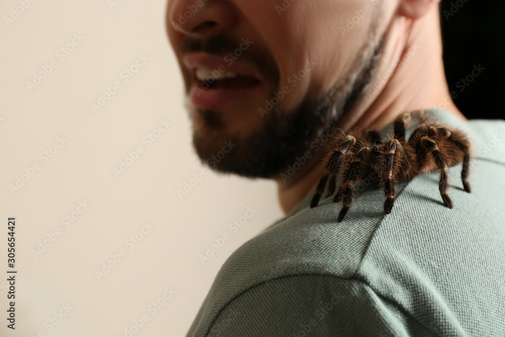 Scared man with tarantula on beige background, closeup. Arachnophobia (fear of spiders) Scared man with tarantula on beige background, closeup. Arachnophobia (fear of spiders)