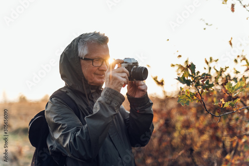 Old man taking photo in nature. Mature man taking pictures of the forest in fall.