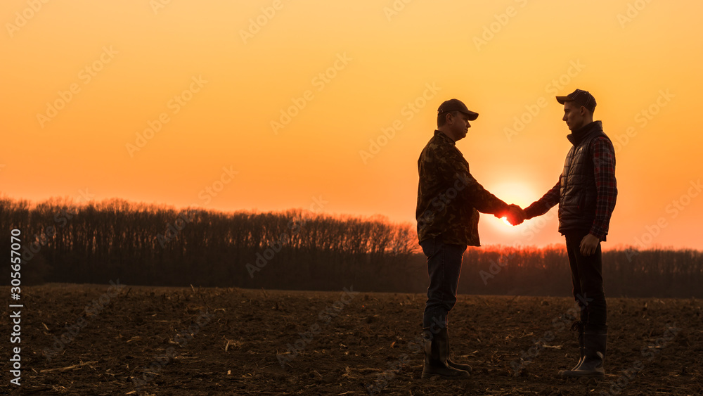 Two farmers shaking hands on a plowed field