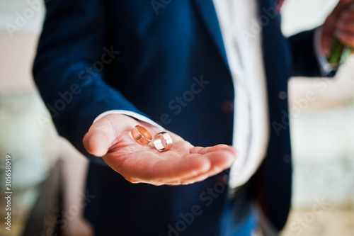 Morning of the groom preparation. Young and handsome groom hold wedding rings on hand.