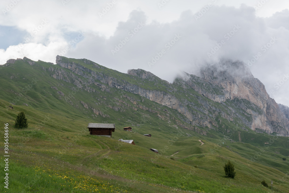 Landscapes of mountain and grassland with small wooden lodge in Seceda, with clouds and blue sky, in Dolomites mountain range in summer