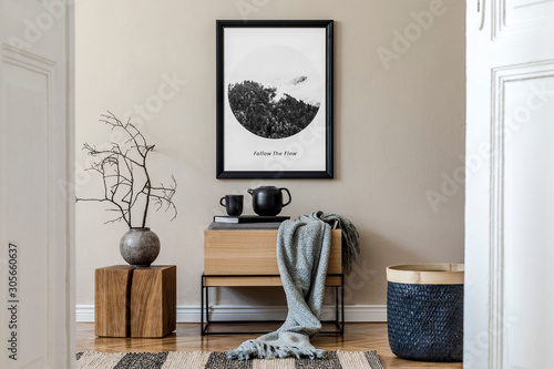 Принти на полотні Modern scandinavian living room interior with black mock up poster frame, design commode,  leaf in vase, black rattan basket, books and elegant accessories