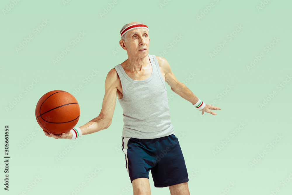Senior man wearing sportwear playing basketball isolated on green background. Caucasian man in great shape stays active and sportive. Concept of sport, activity, movement, wellbeing. Copyspace, ad.
