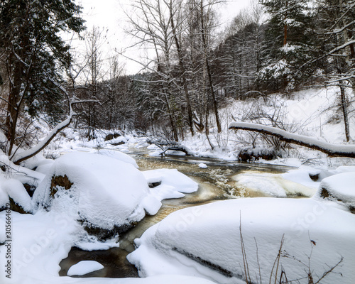 Freezing small river. Banks with trees covered with snow