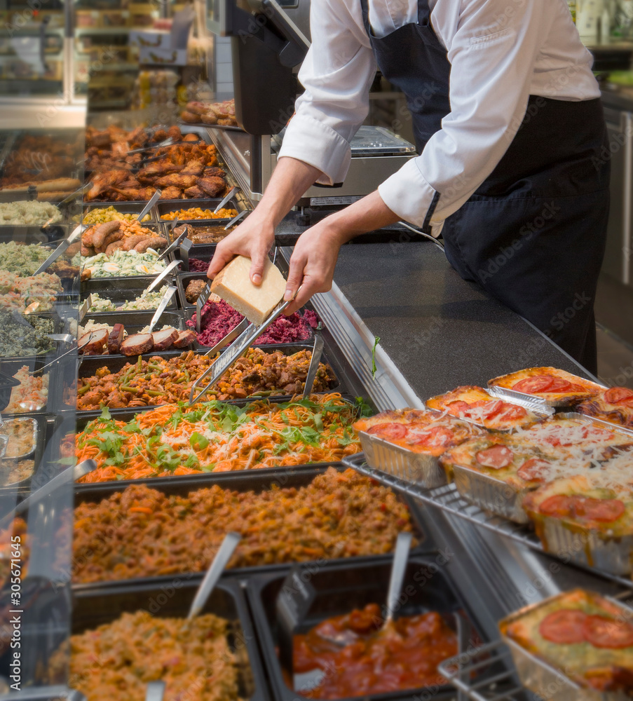 Grating cheese. Rasping cheese in delicatessen shop. Deli. Fresh food in showcase. Shopkeeper.