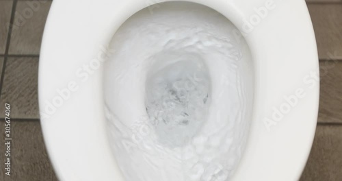 From above clean water flushing in white toilet in public water closet close up