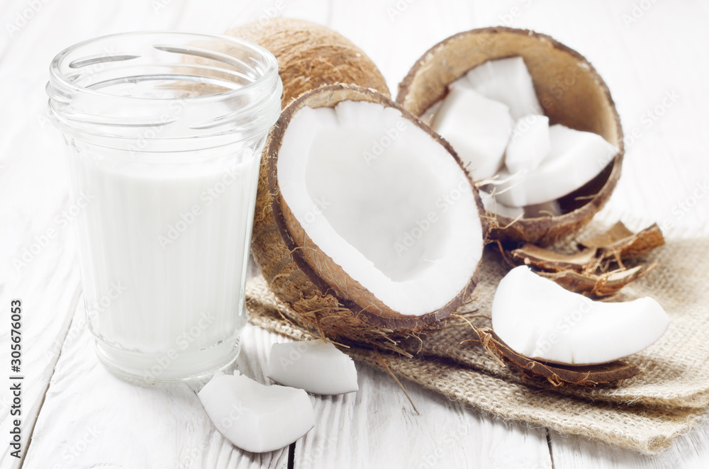 Mason jar of milk or yogurt on hemp napkin on white wooden table with coconut aside Mason jar of milk or yogurt on hemp napkin on white wooden table with coconut aside