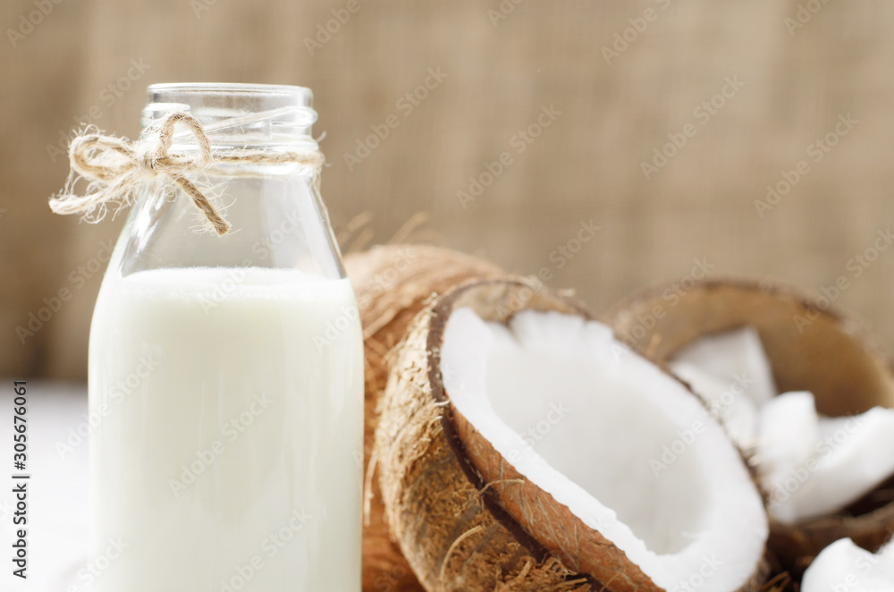 Milk or yogurt in glass bottle on white wooden table with coconut aside Milk or yogurt in glass bottle on white wooden table with coconut aside