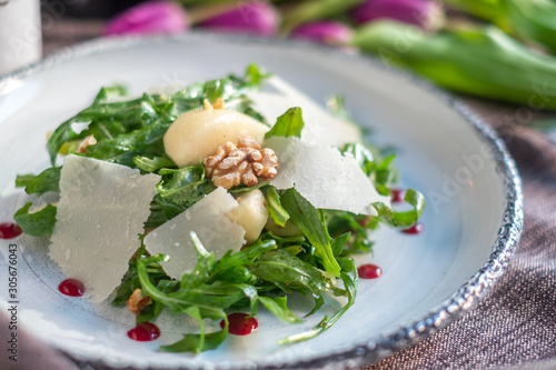 Fresh Salad with arugula, Parmesan cheese, potatoes and nuts on a white plate.