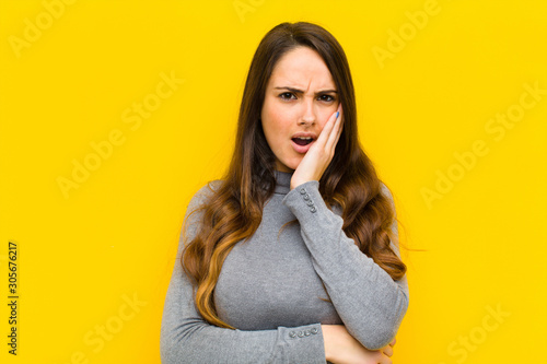 young pretty woman open-mouthed in shock and disbelief, with hand on cheek and arm crossed, feeling stupefied and amazed job or business concept photo