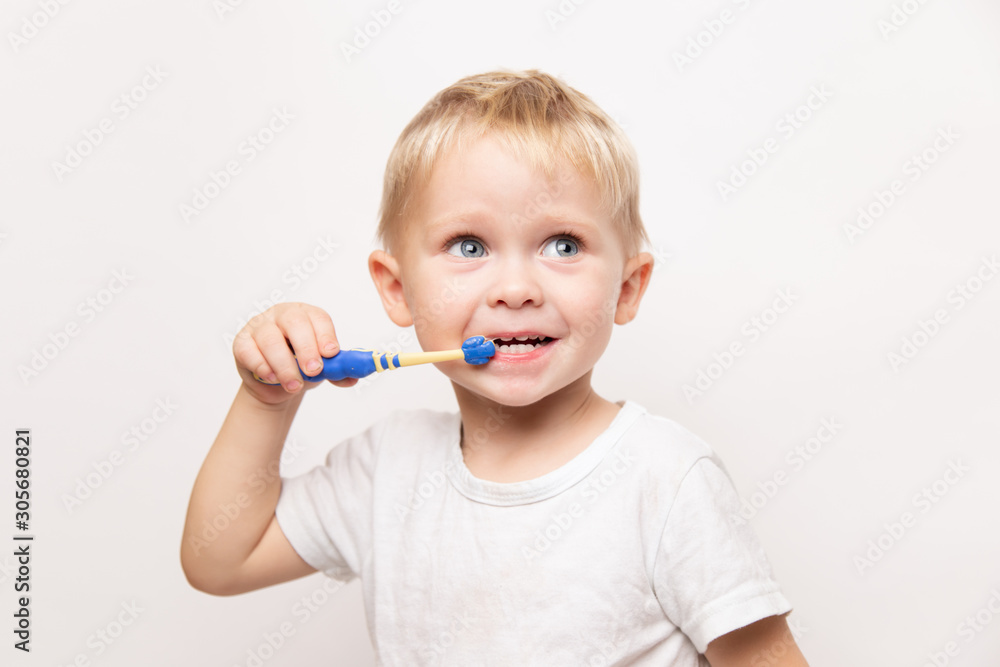 little cute caucasian blond blue-eyed boy in a white t-shirt brushes his teeth on a white background little cute caucasian blond blue-eyed boy in a white t-shirt brushes his teeth on a white background