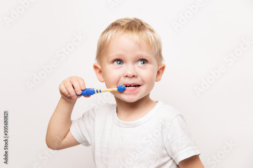 little cute caucasian blond blue-eyed boy in a white t-shirt brushes his teeth on a white background