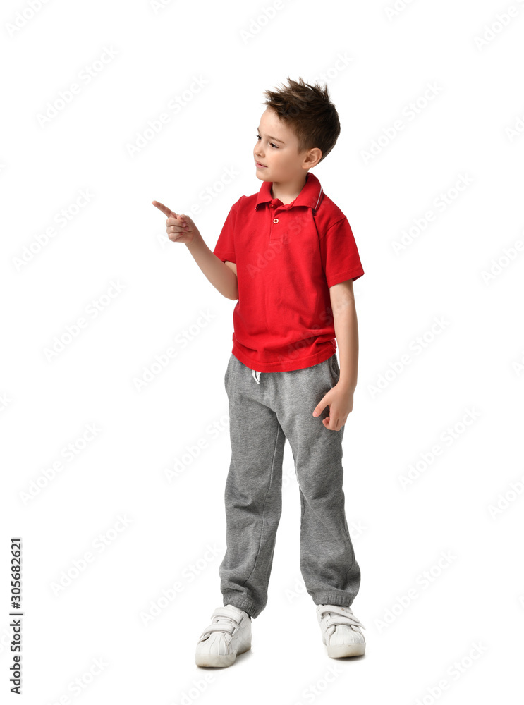 Young full body boy kid in red polo t-shirt standing pointing one finger at the corner isolated on white