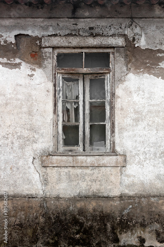 Window with rotten wood frame and broken glass on derelict building with plaster coming off a white wall with red bricks underneath. Decay. Background. Game scenario textures. Grunge © Ana
