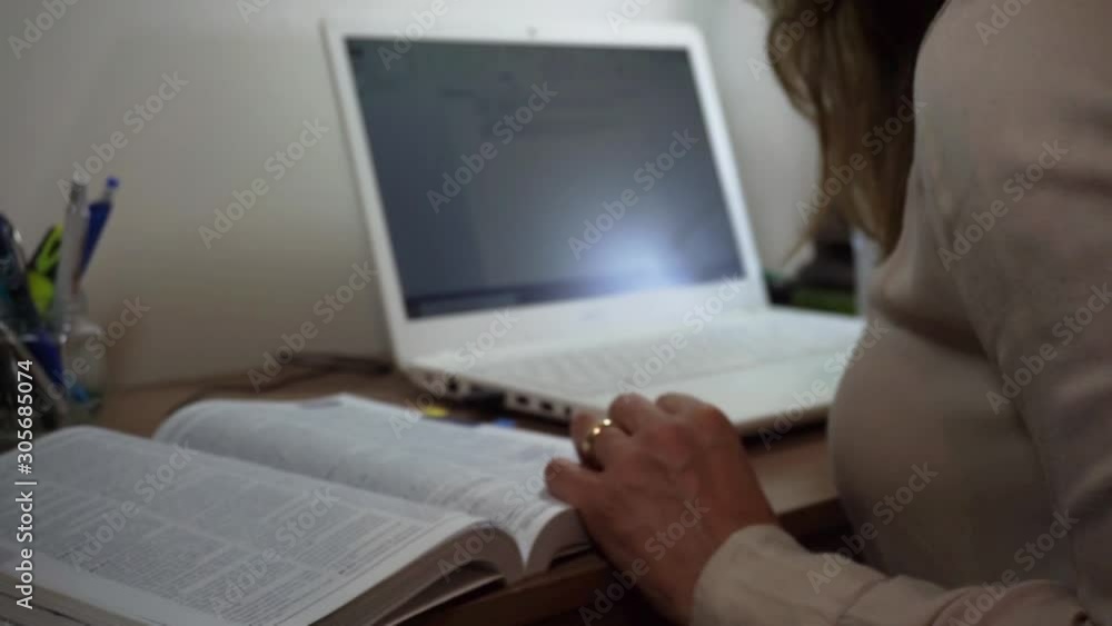 Uma mulher no escritório lendo livro e digitando no computador 